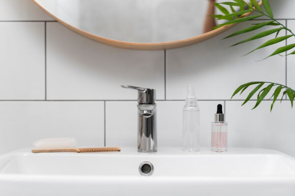 Chiuvetă modernă cu produse cosmetice, oglindă și plantă verde